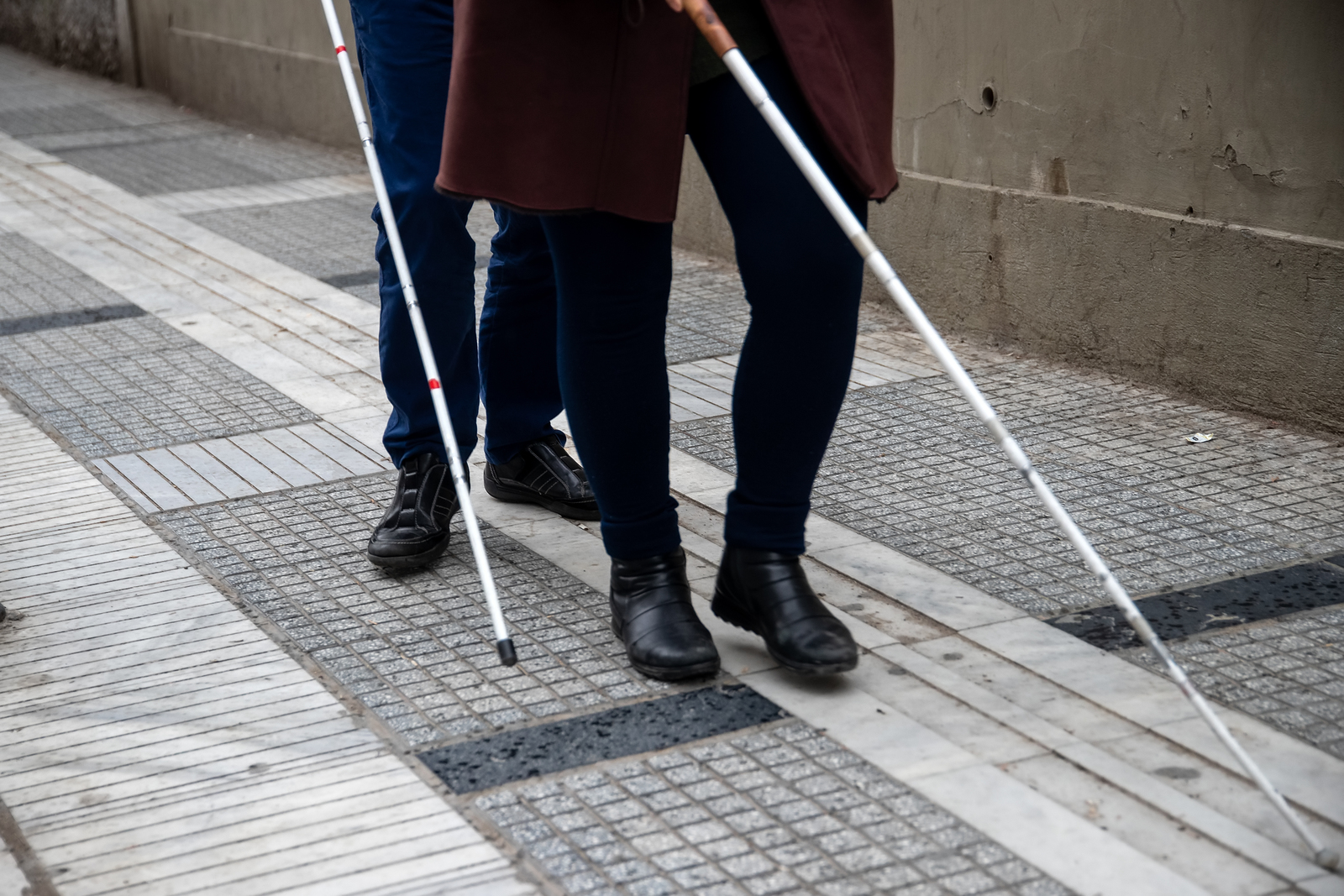 blind man and woman walking on the street using white canes.