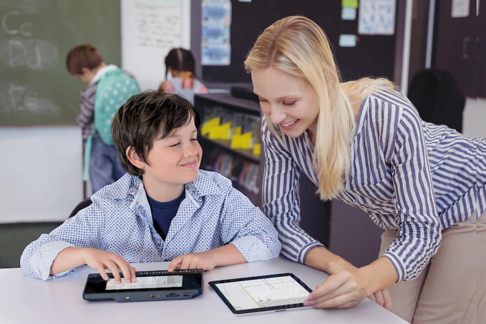 A student in a classroom setting using a Humanware Braillenote Touch, with another student looking on.